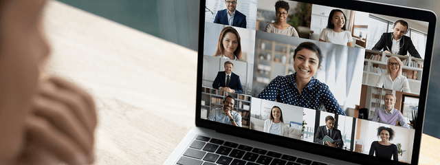 A person looking at a laptop showing a virtual meeting with many smiling participants.