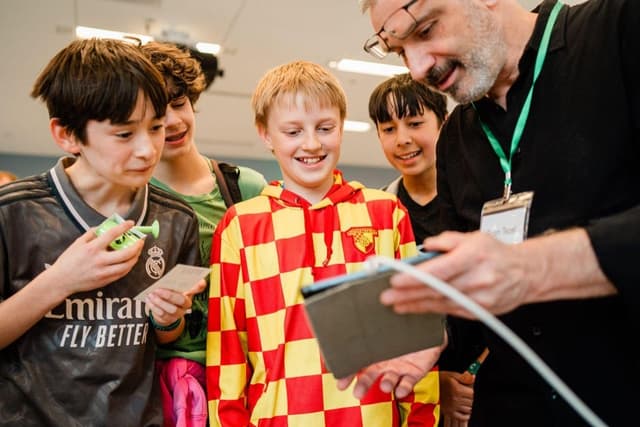 Four young people smiling and looking at data on an iPad from MIT App Inventor with an instructor.