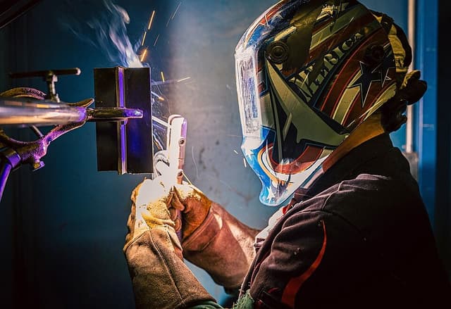 A man in a welding helmet is actively welding metal pieces together.