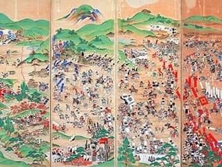 Hundreds of men, some on horseback, battle in the midst of a green hill terrain.