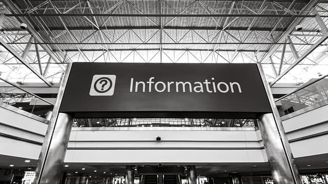 Black and white image of an information desk sign in a public place. 