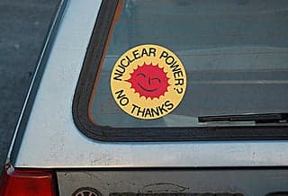A yellow and red round sticker about anti-nuclear power is on the back window of a car.