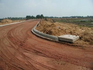 A photograph of a new road being constructed in Vietnam. The photograph shows a recently graded dirt surface as well as curbs and and a drainage system.
