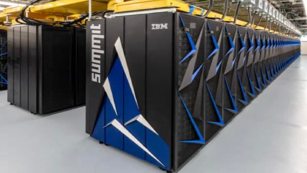A large warehouse-like room filled with rows of connected electronic modules, with the Summit logo and the IBM logo printed on one end of the first row.