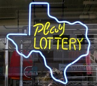 A photograph of a store window with an outline of the state of Texas in neon. Inside the outline are the words "Play Lottery."