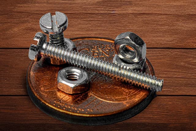 A close-up photo of nuts and bolts on a shiny copper penny, set on a wood surface.