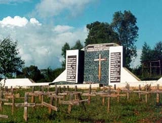 Image of a cemetery and memorial for the Rwandan genocide. A myriad simple crosses stand in front of a memorial.
