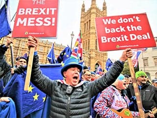 In the midst of a crowd, a man carries signs with the words: “The Brexit Mess!” and “We Don’t Back the Brexit Deal.”
