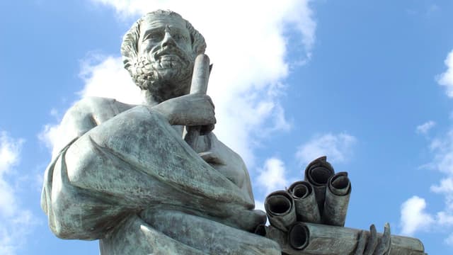 A statue of a strong-jawed young man, carrying scrolls in his hands.
