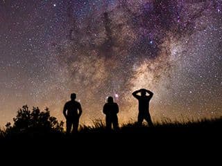 Three silhouetted figures look at a star-filled sky.