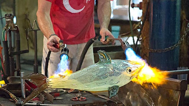 A pair of arms points two torches towards a glass model.