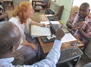 A translator and interview subject sign to one another as an anthropologist watches.