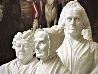 A gleaming white marble structure featuring busts of three mature women with solemn expressions on their faces.