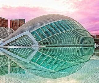 A modern structure made of glass and steel. It curves upwards into a half circle and is reflected in the pool around it.