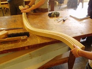 A wood-bending demonstration. Three students bending wooden strips with their hands.