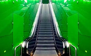 A photo of an escalator with green walls.