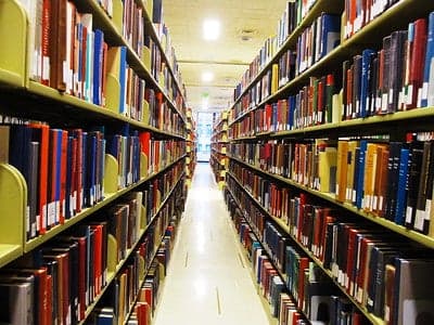 A library aisle with shelves full of assorted books on both sides.